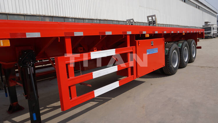 The flatbed trailer has a spare tire frame, a toolbox
